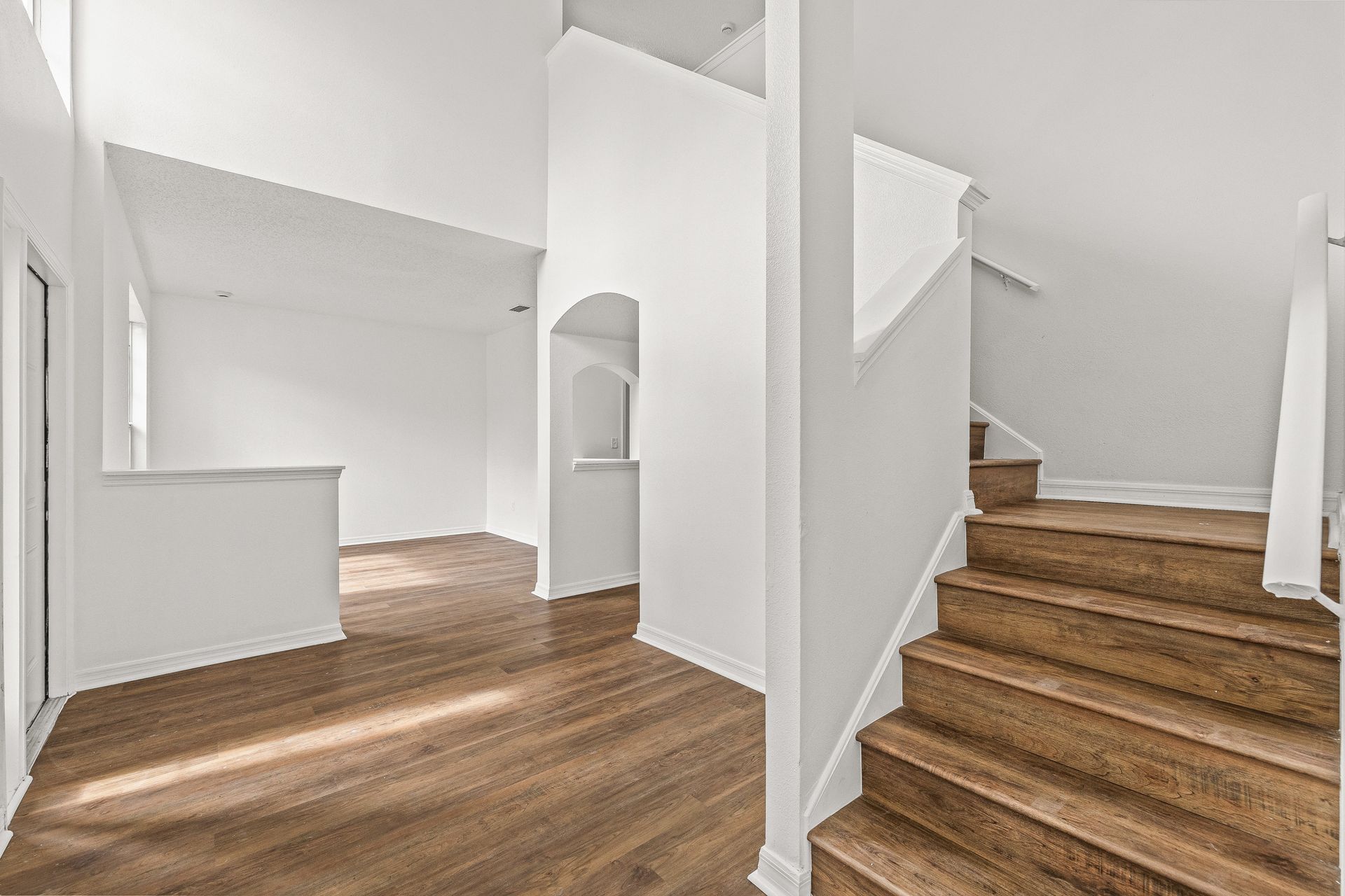Bright white hallway with wood floors, staircase, and open living area.