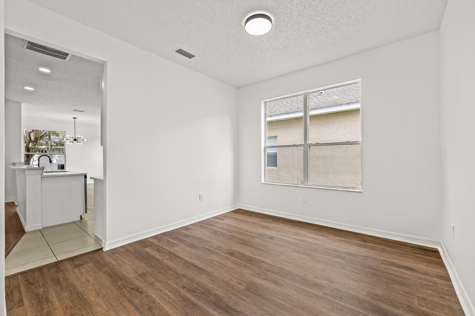 Empty white bedroom with wood flooring, a window, and an open doorway to a bathroom area