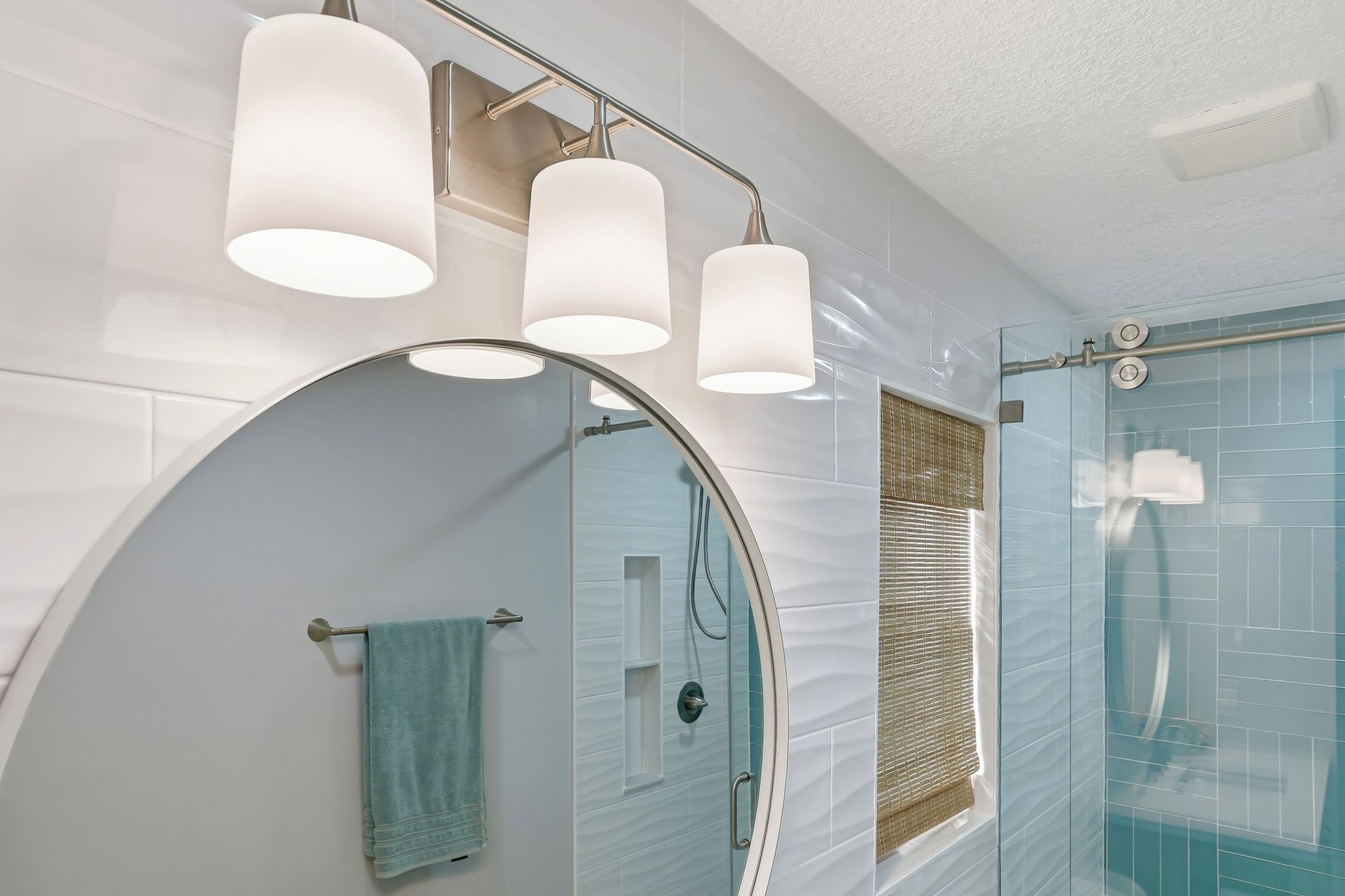 Bright bathroom with a round mirror, white vanity lights, and glass shower enclosure with blue tiles