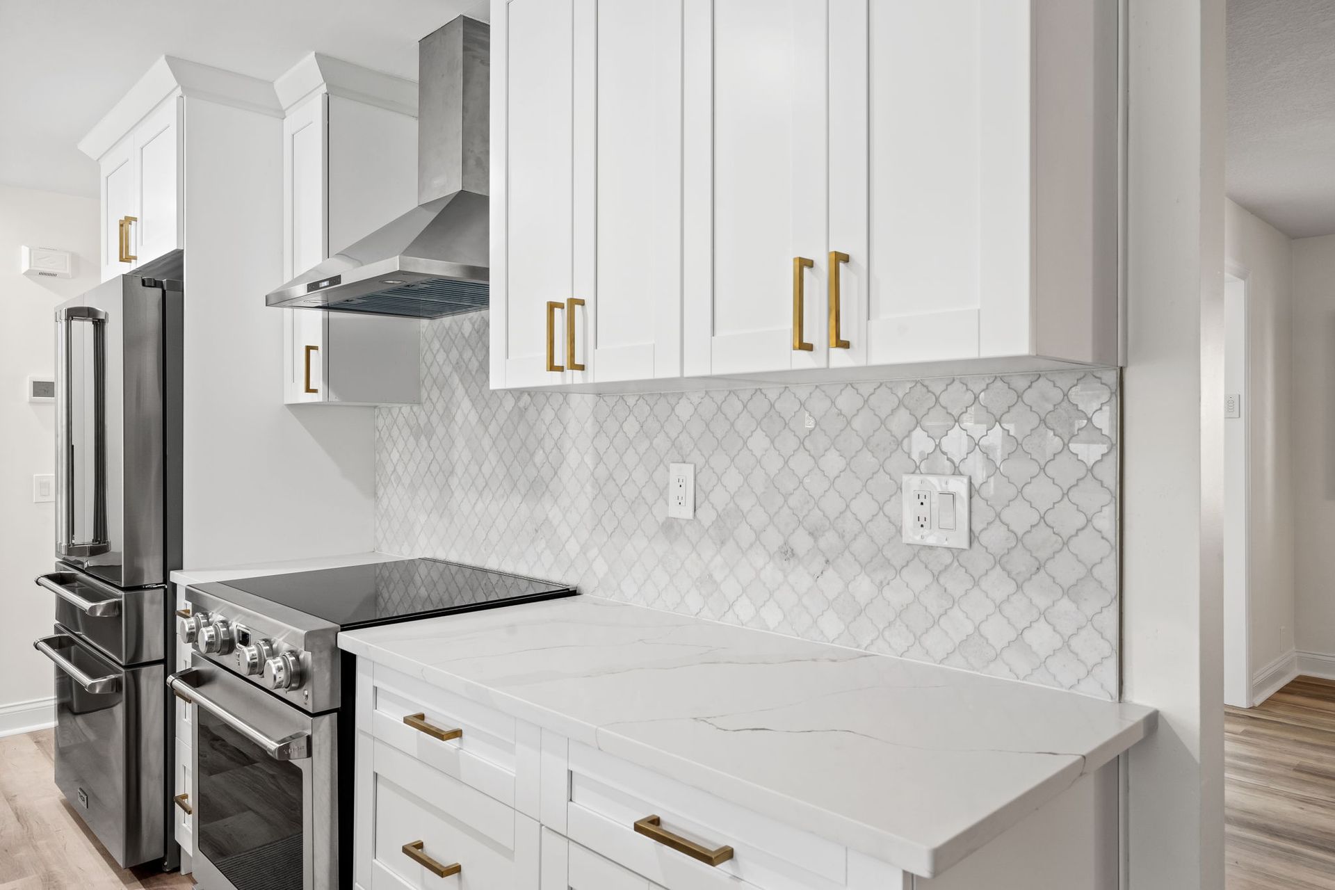 Bright white kitchen with gold handles, stainless appliances, and gray herringbone backsplash