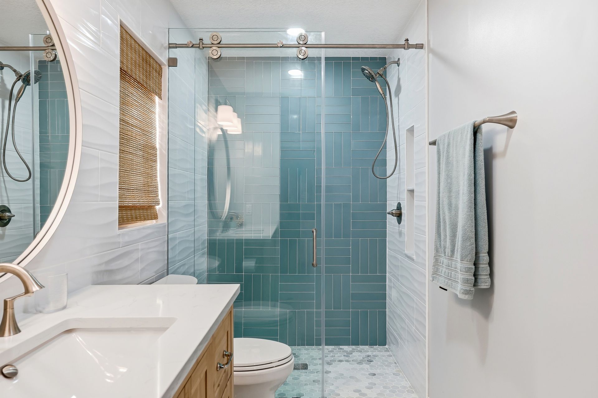 Modern bathroom with glass shower, white vanity, round mirror, and light blue tile accents