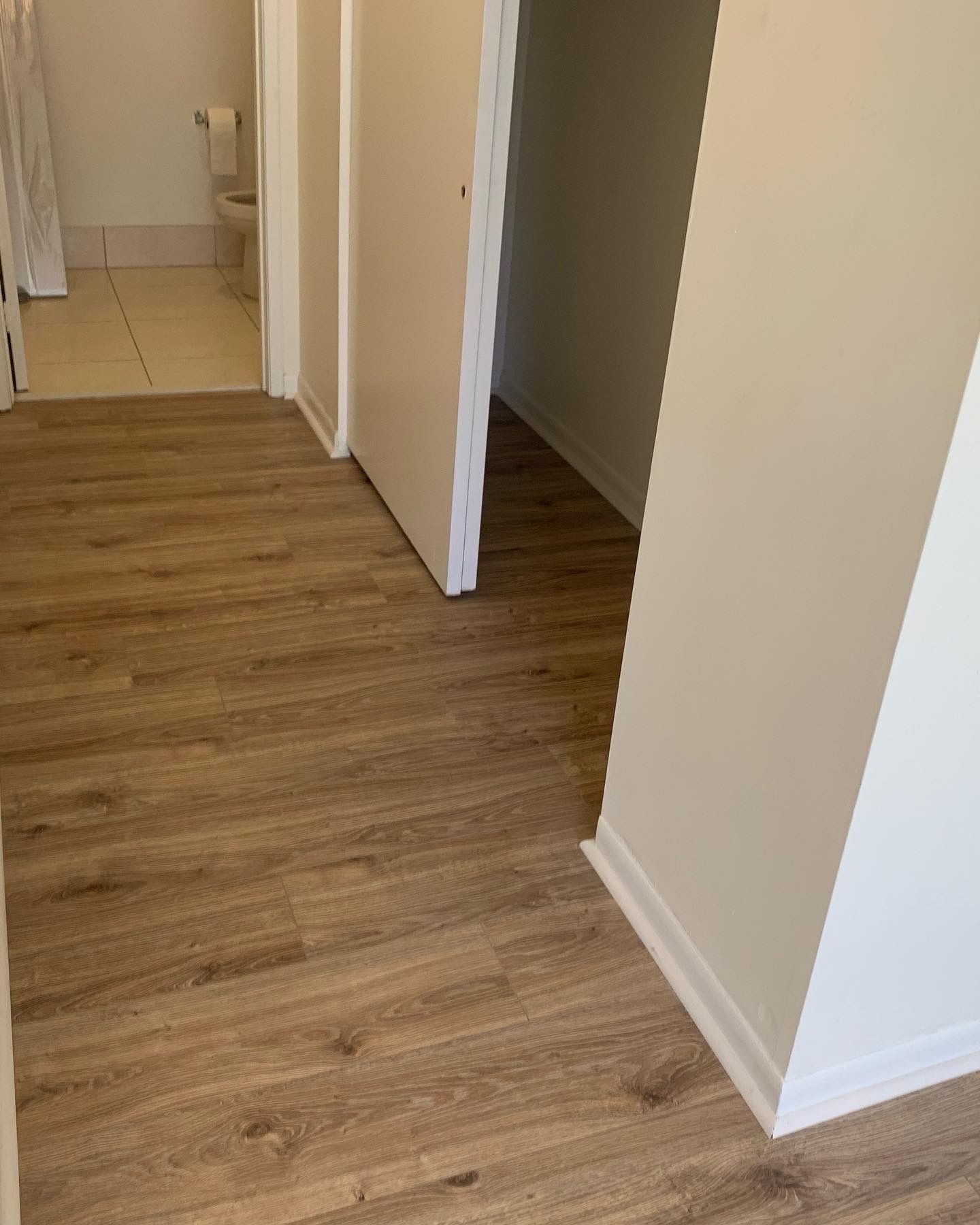 Empty hallway with wood flooring, white walls, and open doorways.