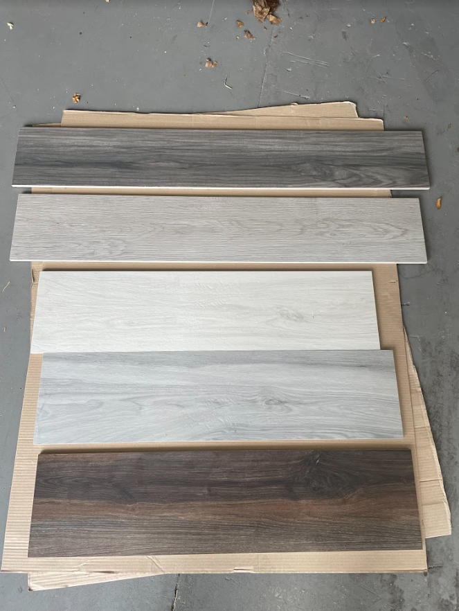 Five wood-look flooring planks in gray, white, and brown laid vertically on a gray surface