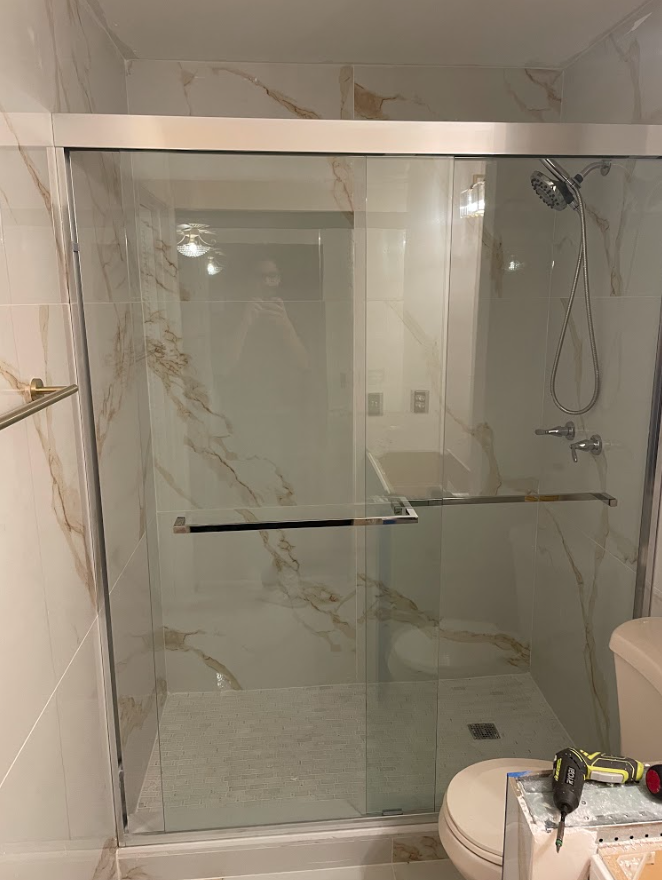 Bathroom with glass shower enclosure, marble-look tile walls, and handheld showerhead