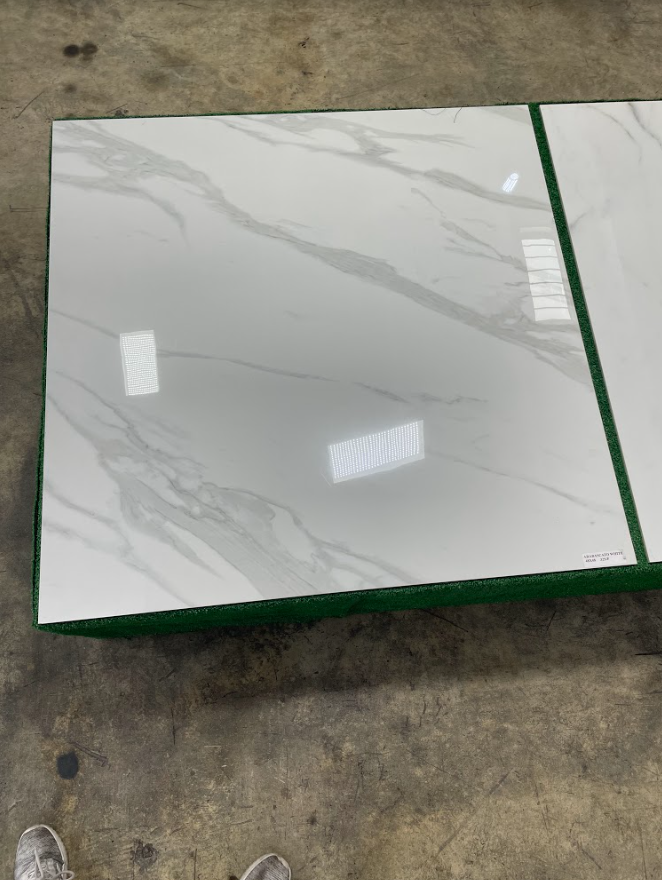 White marble-look tile on a concrete floor, wrapped with green edging and reflecting overhead lights