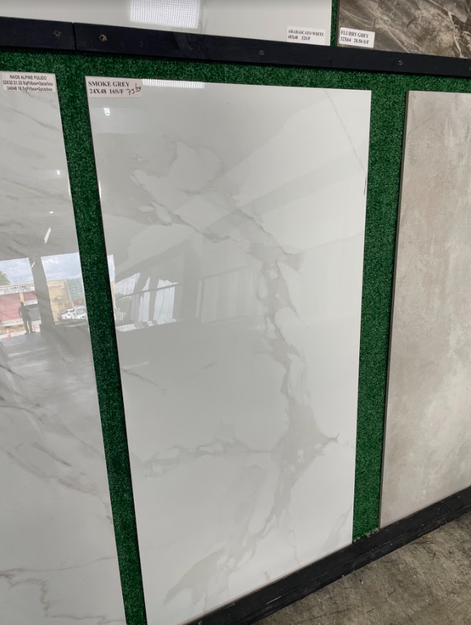 White marble-look floor tile display with gray veining, framed by green trim in a showroom.