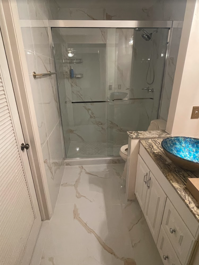 Bathroom with glass shower, white cabinets, and marble-patterned floor tiles