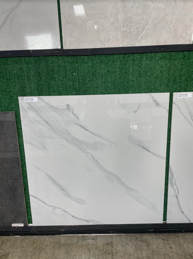 White marble-look tile sample displayed against a green turf backdrop with gray stone tiles above and below