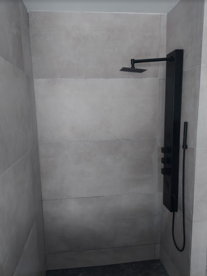 Minimal tiled shower stall with a black rain showerhead and handheld sprayer on the right wall