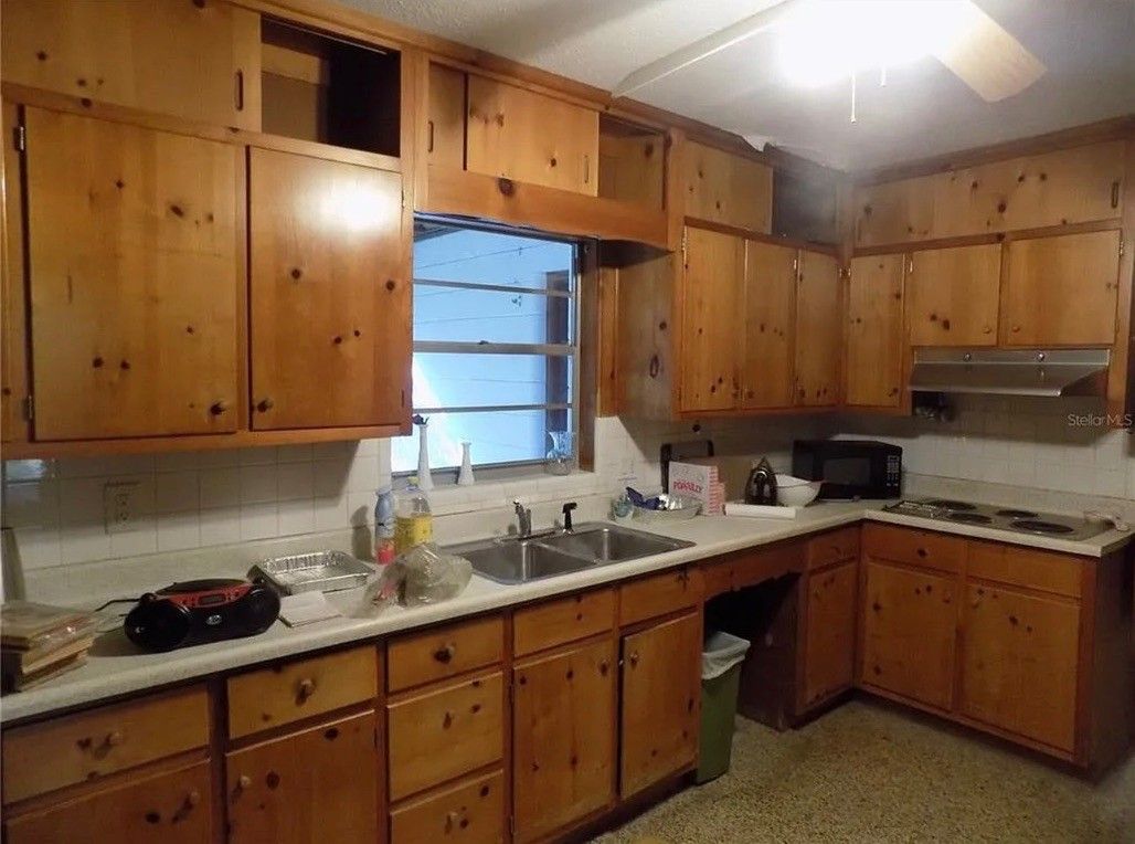Wood-paneled kitchen with wooden cabinets, white countertops, and a central sink under a window.