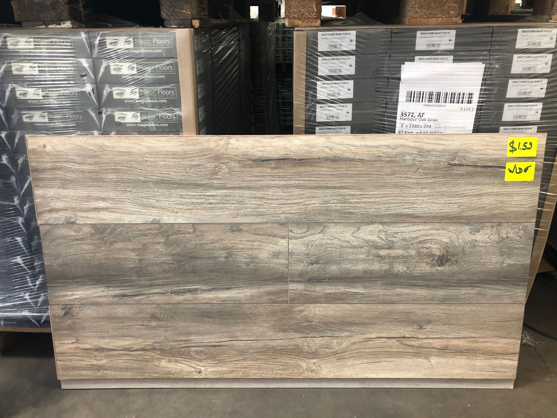 Wood-look tile slab displayed in a warehouse aisle with stacked boxes behind it.