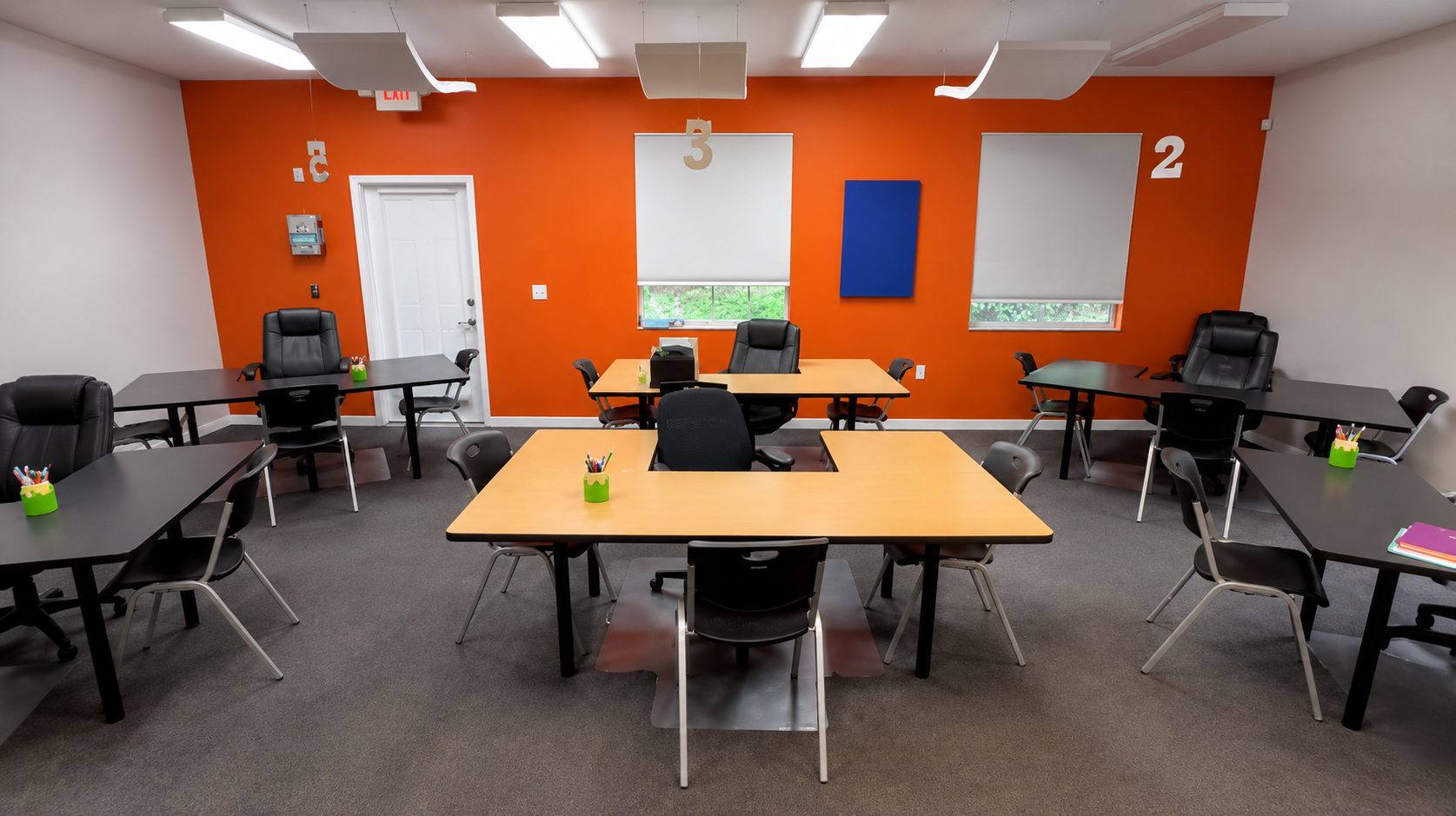 Bright orange classroom with tables, chairs, and whiteboards in a computer lab setup.