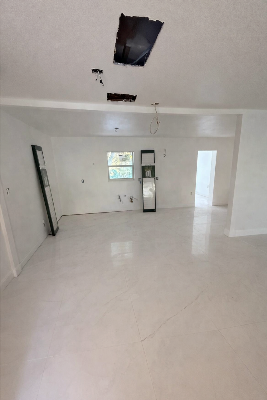 Empty white room under renovation with tiled floor, exposed ceiling openings, and a doorway in back