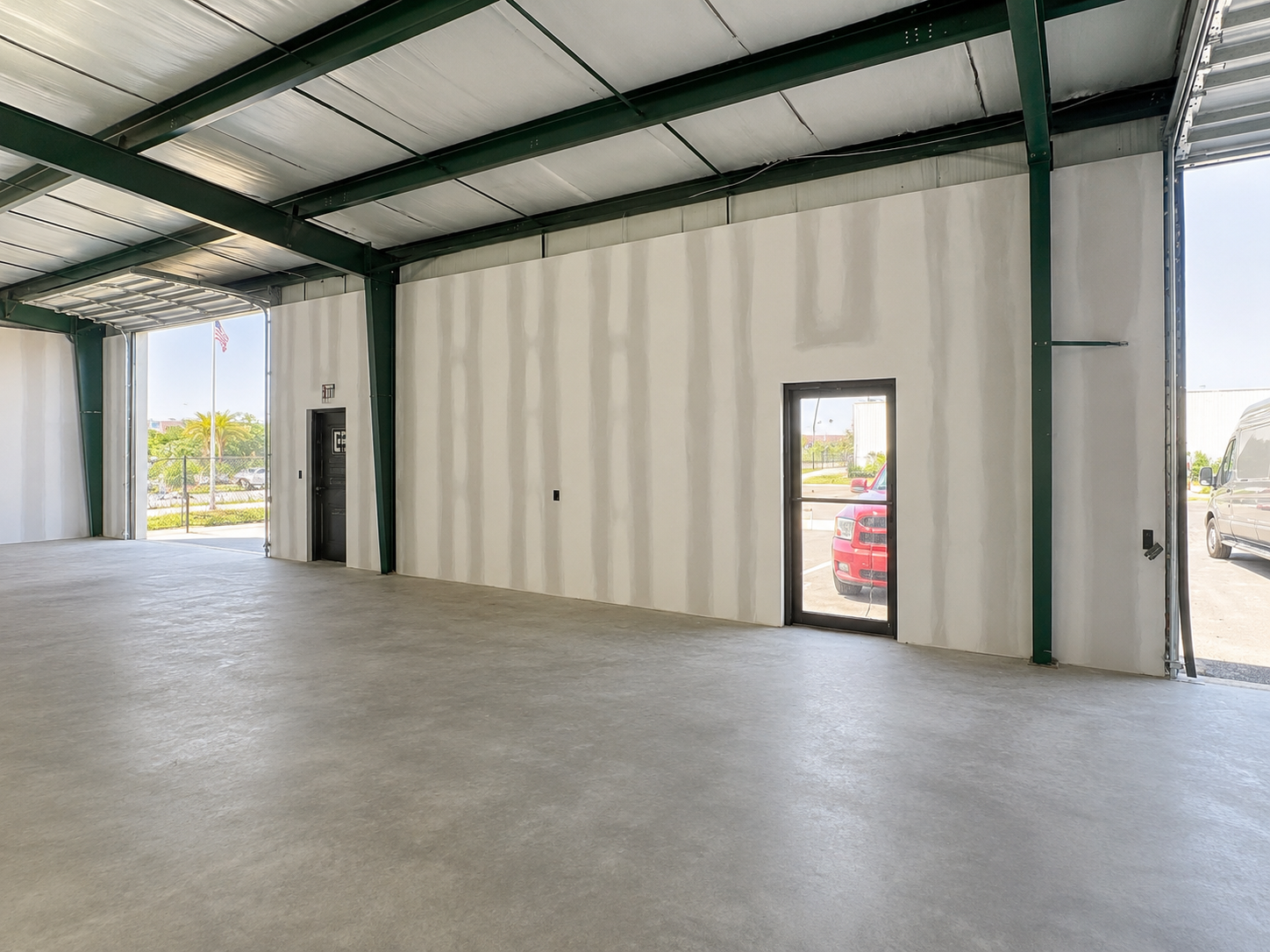 Empty industrial warehouse interior with concrete floor, green steel beams, and open doorways