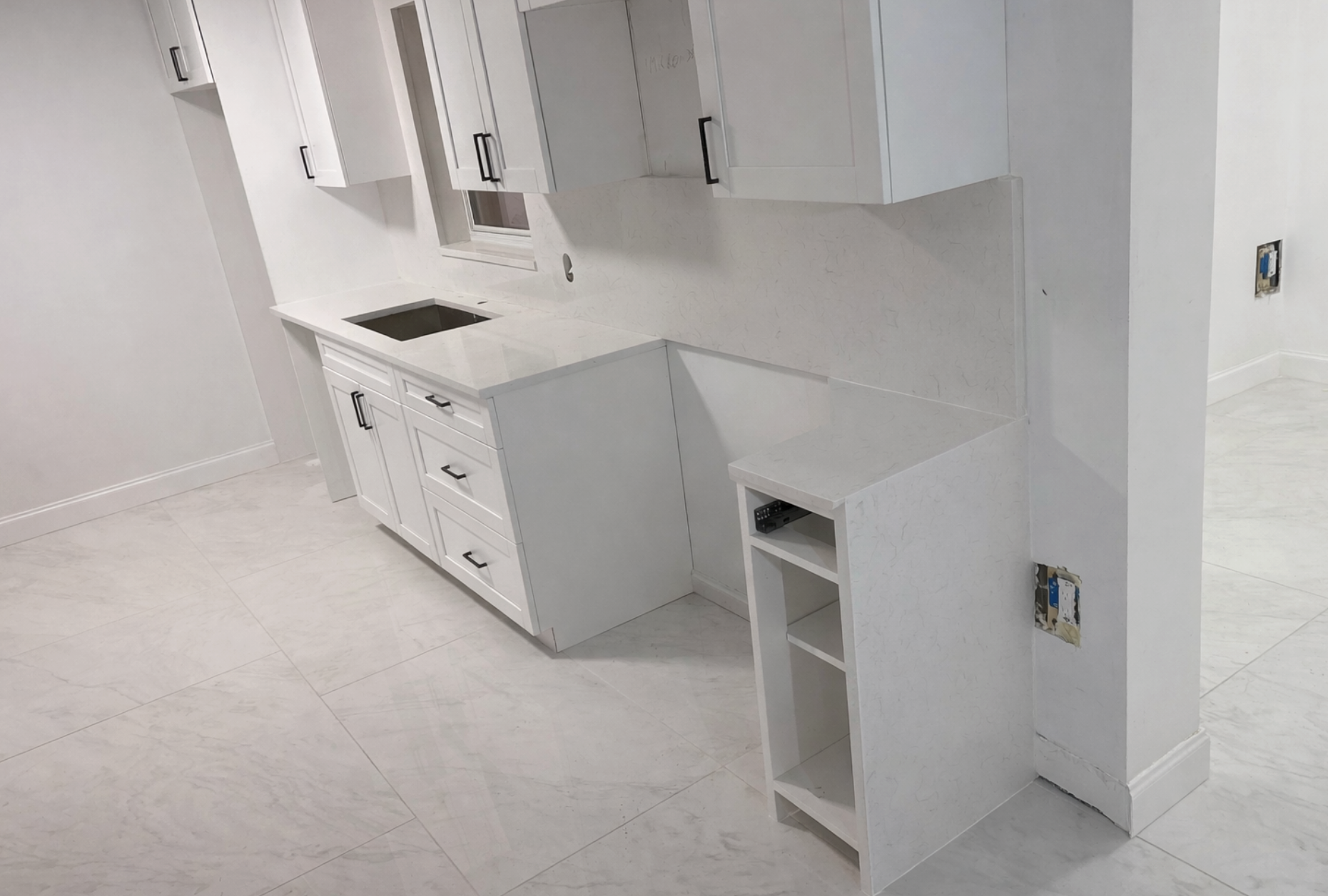 Empty white kitchen under construction with cabinets, countertop, and unfinished wall outlets