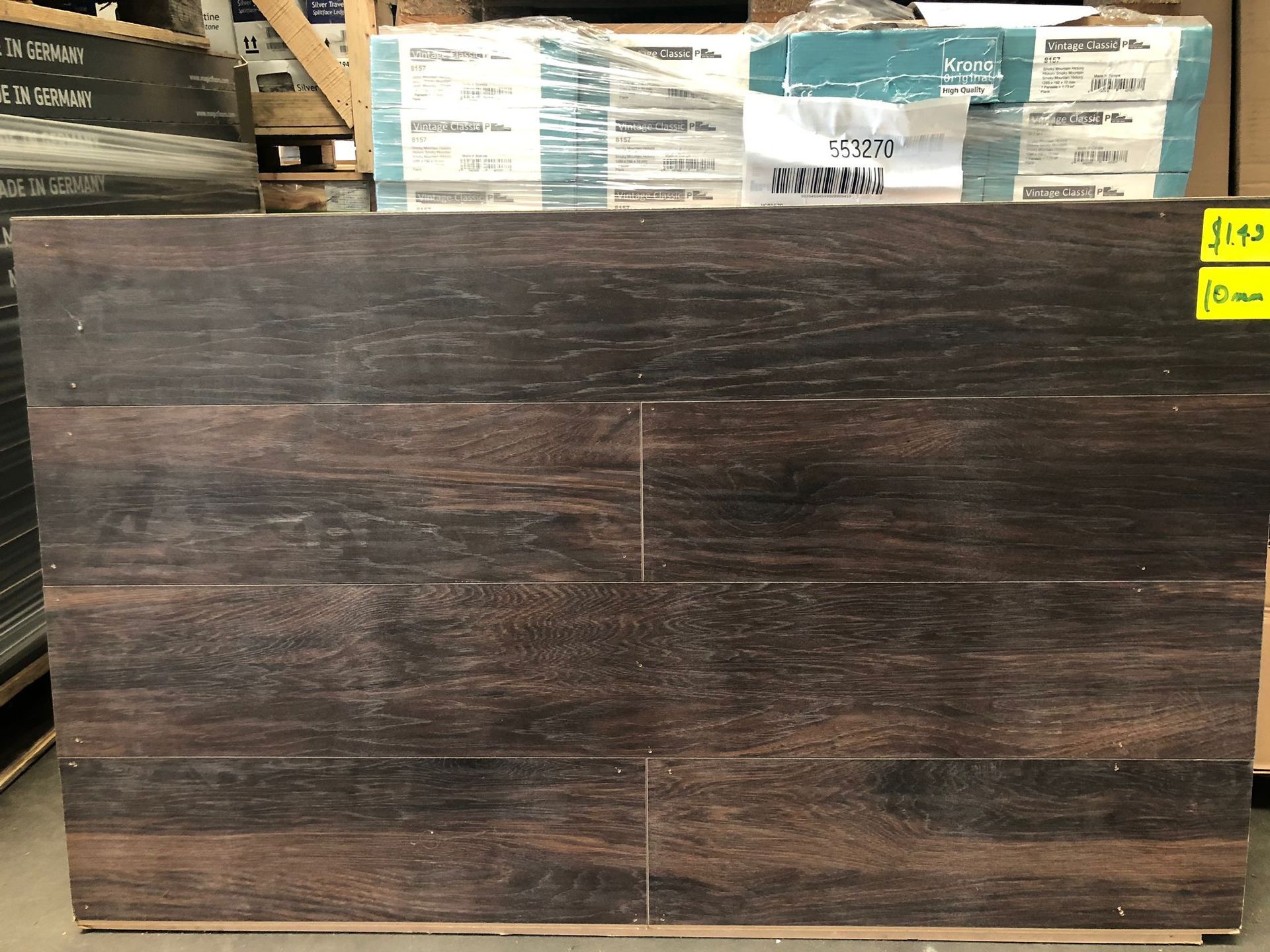 Dark wood-look laminate panel displayed in a warehouse aisle with product stacks behind it.