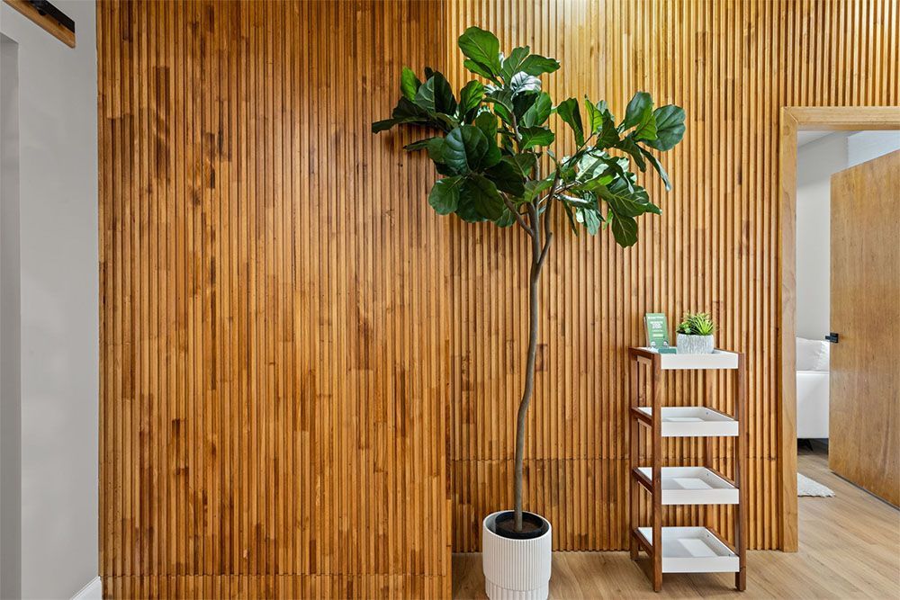 Tall potted tree beside a small white shelf against a wooden slat wall in a modern interior