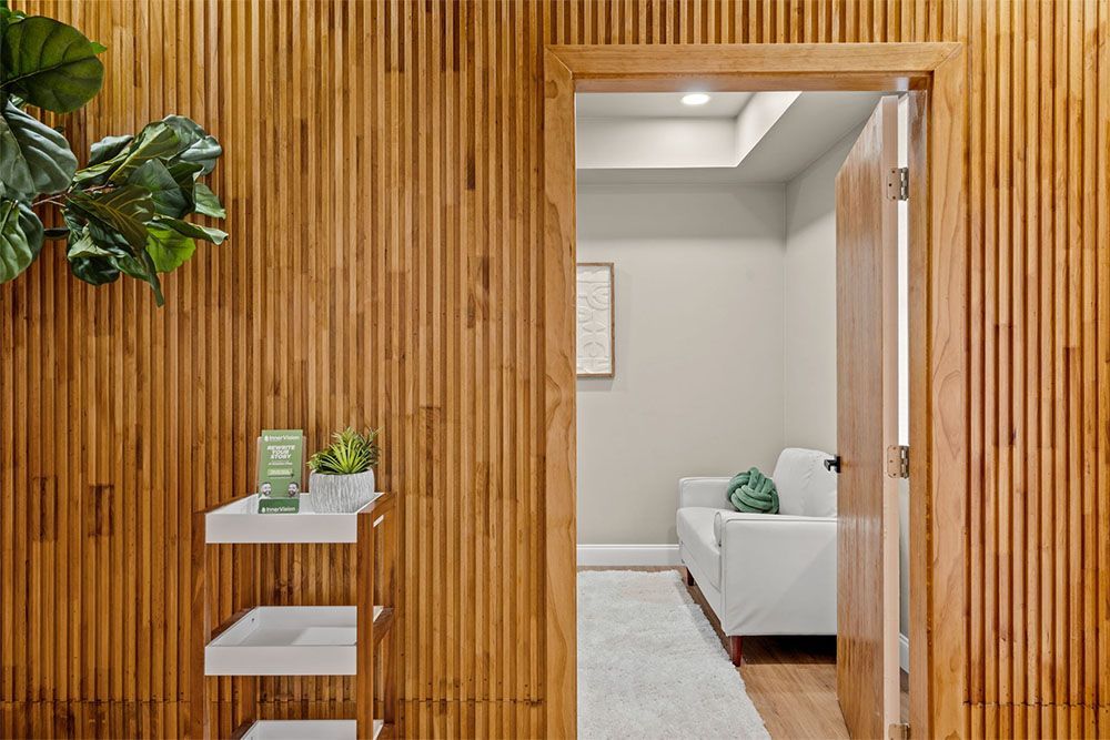 Wood-slat wall with doorway to a bright living room; small shelf and plant in the foreground.