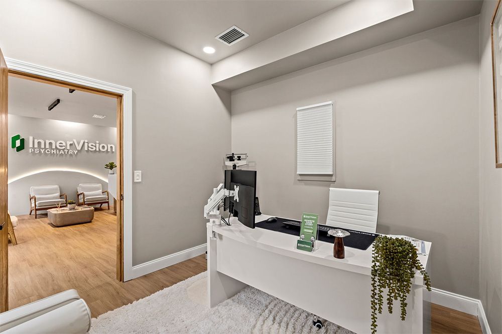 Modern clinic reception area with white desk, gray walls, and doorway to a furnished room