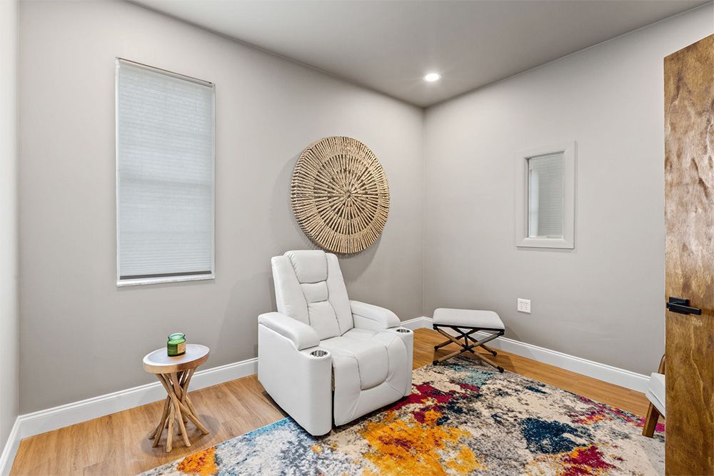 Modern living room with a white recliner, colorful rug, side table, and wall decor in neutral tones