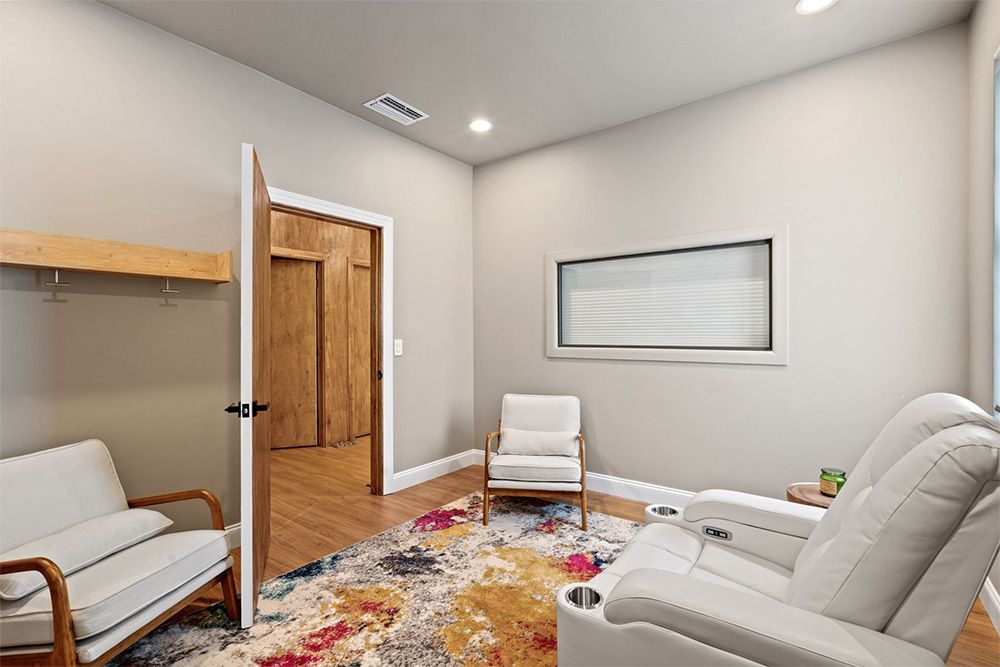 Small waiting room with white recliners, wood doors, a colorful rug, and a framed wall window.