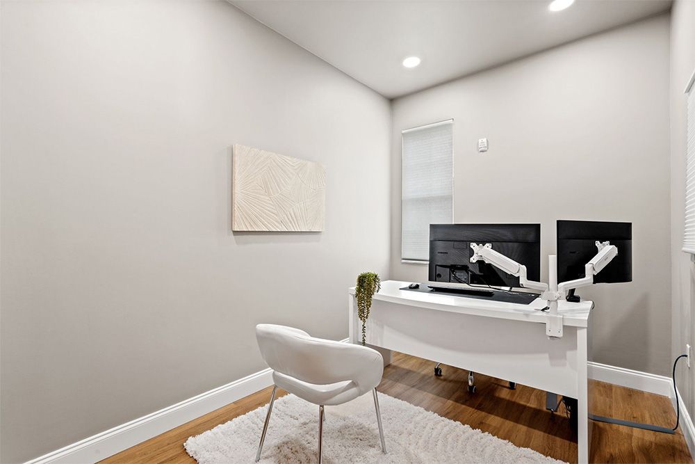 Modern home office with a white desk, chair, computer monitors, and gray walls