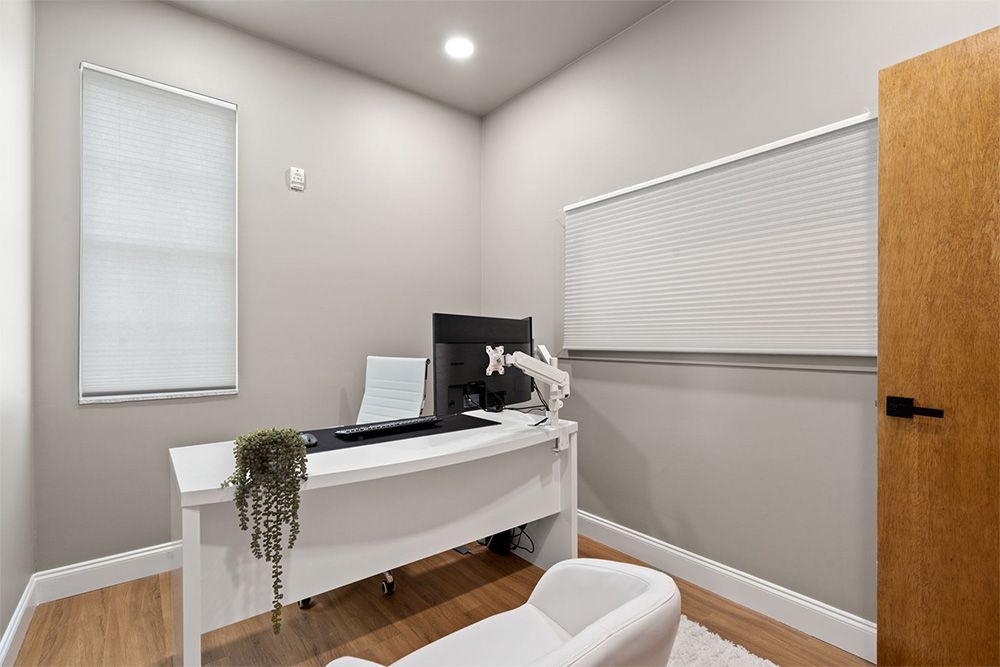 Modern home office with white desk, computer, hanging plant, and closed blinds