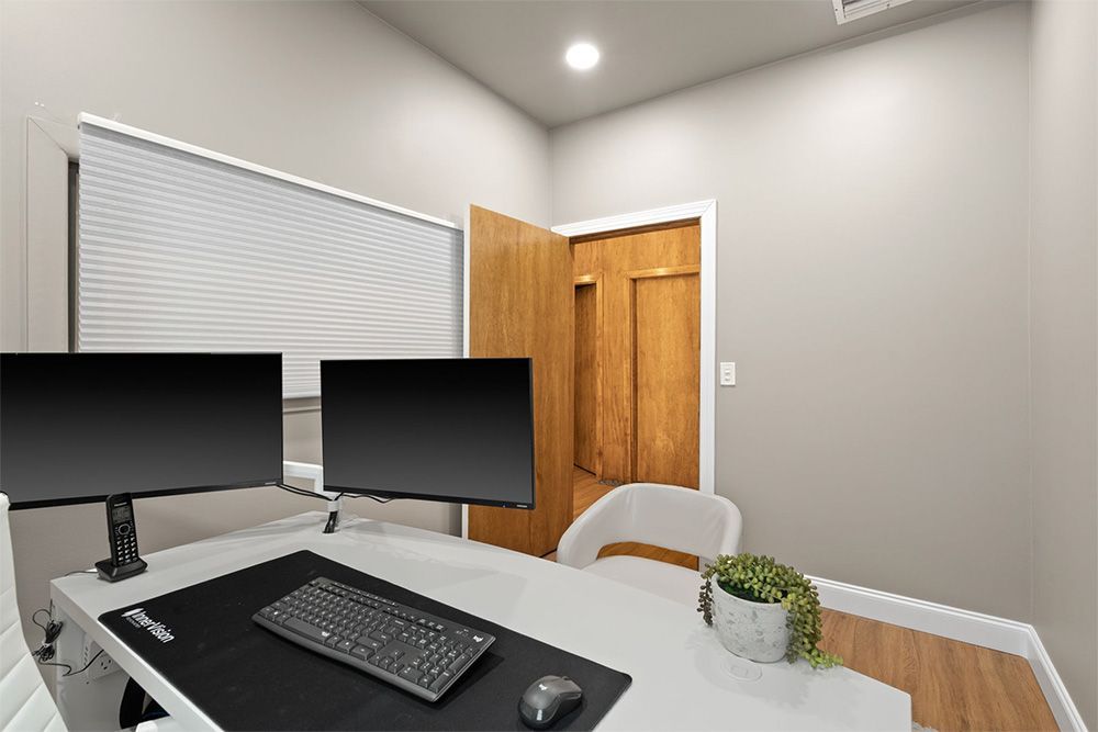 Home office with dual monitors, desk, keyboard, and open door in a gray room