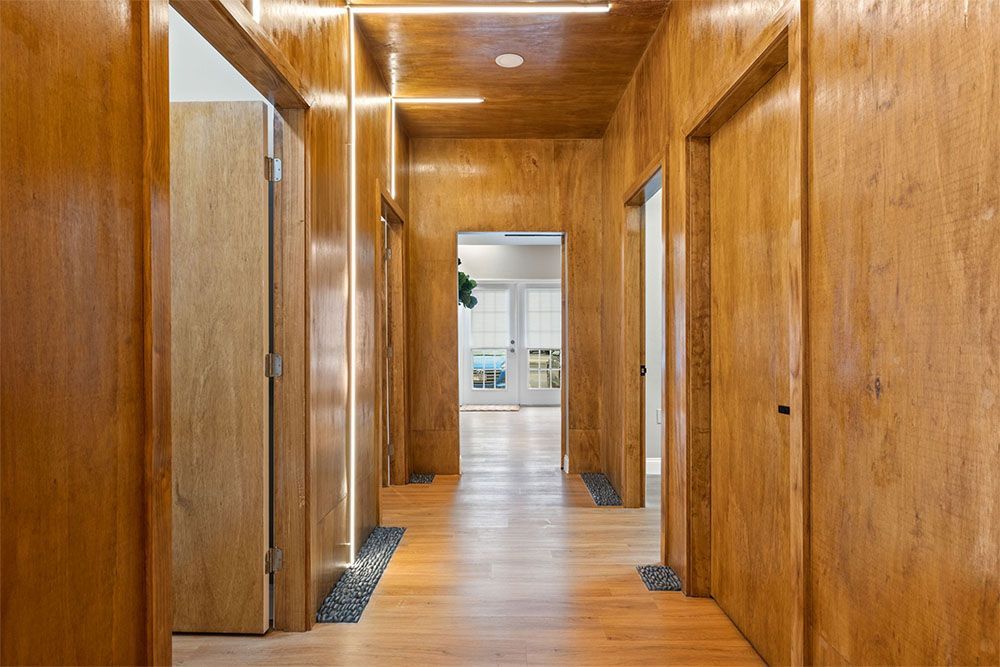 Wood-paneled hallway with doors and a wooden floor, leading to a bright room at the end.