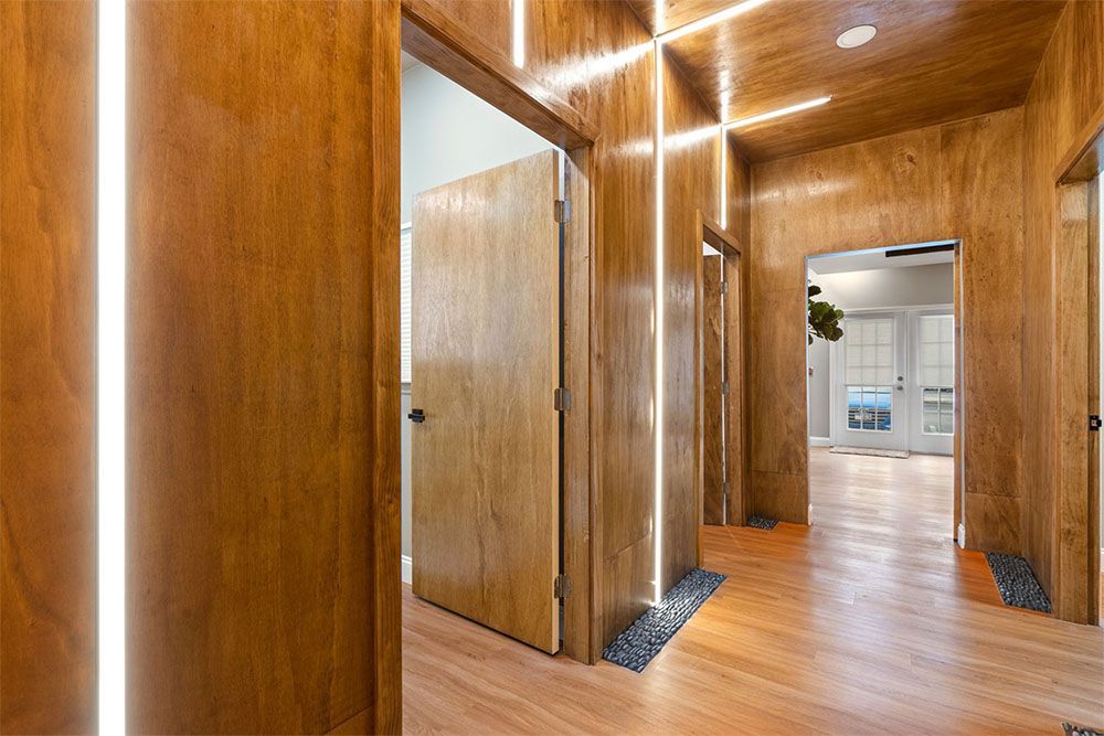 Wood-paneled hallway with recessed lights and open doors leading to a bright room.