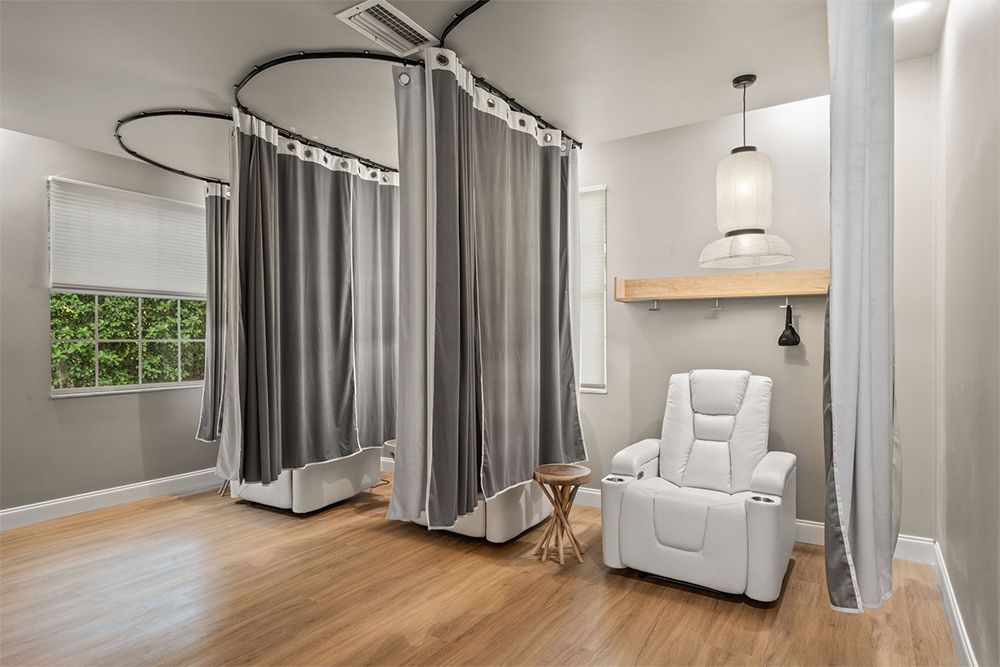 Modern spa room with gray curtains, white recliner chair, hanging lights, and wood flooring