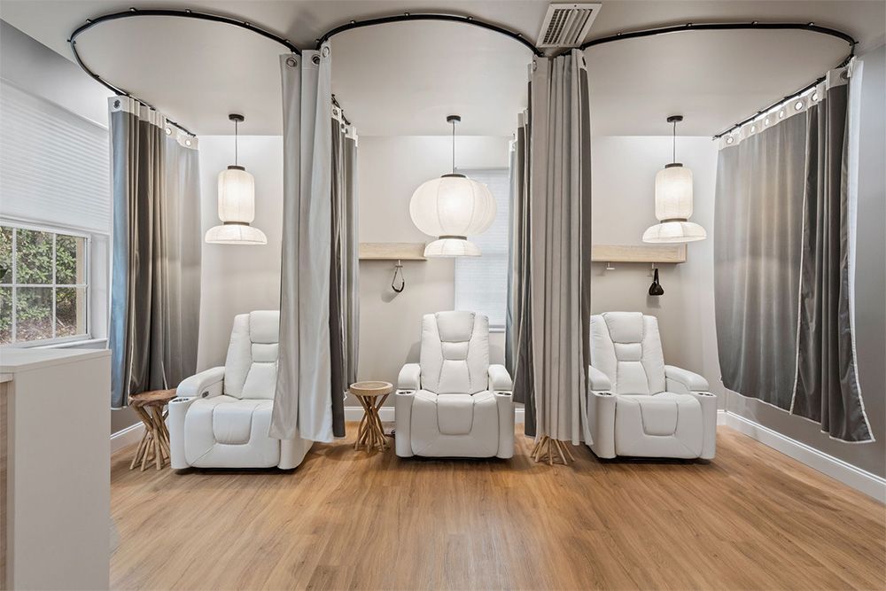 Elegant spa room with three white massage chairs, curtained alcoves, and warm wood flooring