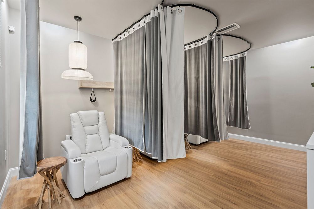 Modern spa room with white treatment chair, curtained booths, and wood floors