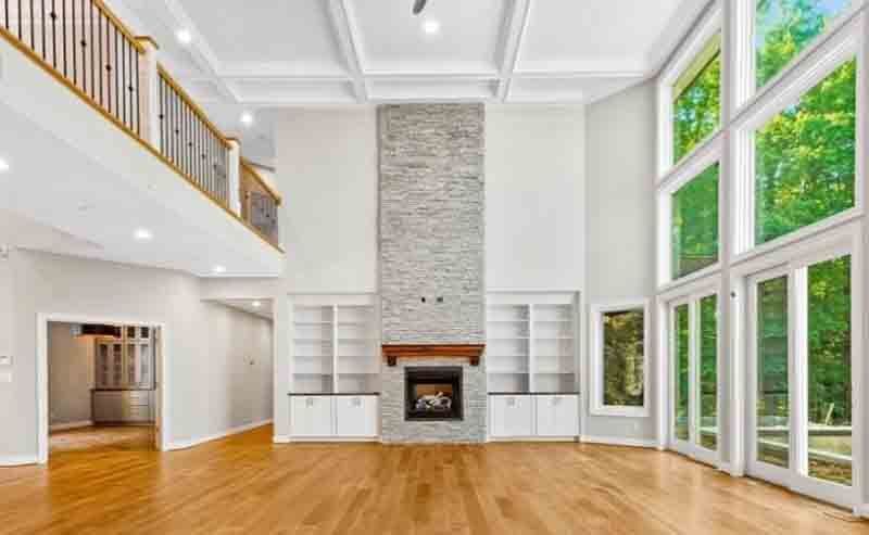 Bright modern living room with hardwood floors, tall windows, and a stone fireplace with white built-ins