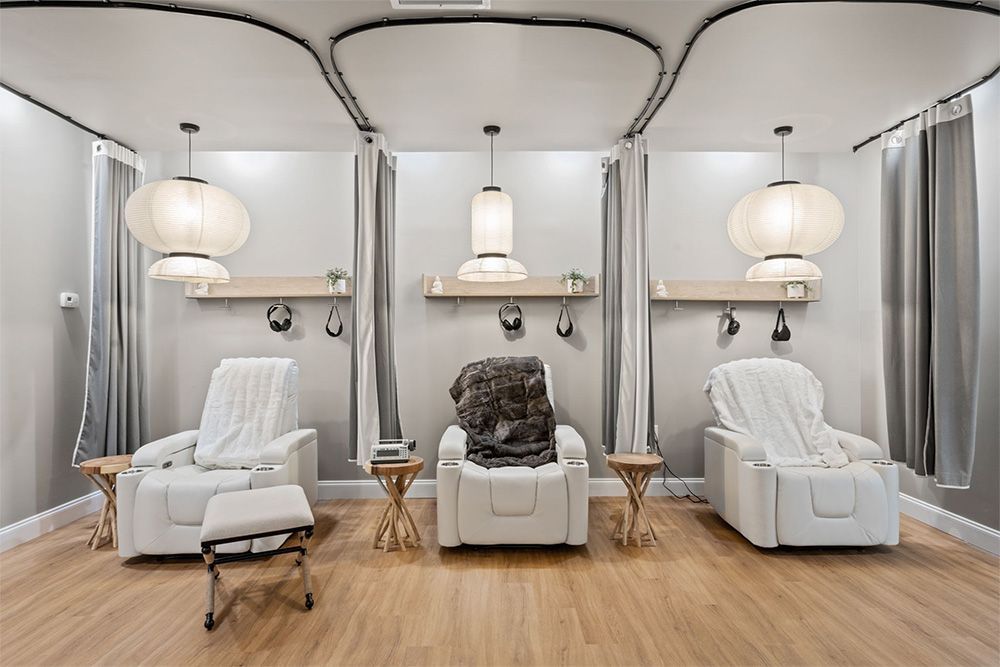 Modern spa room with three white recliners, a black massage chair, soft lighting, and gray curtains