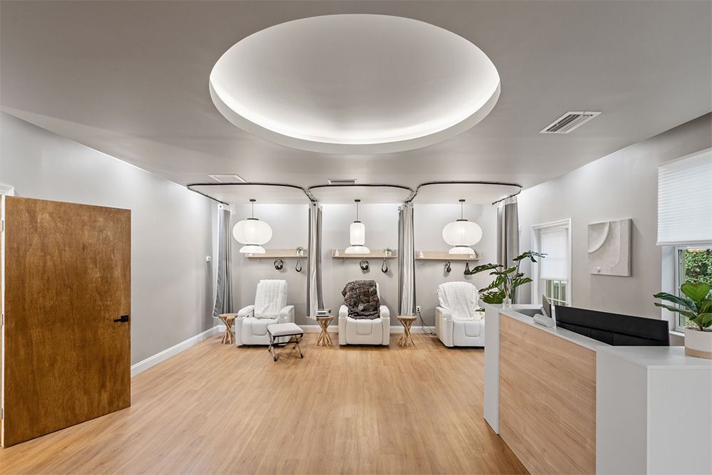 Modern spa reception with white treatment chairs, wood floors, and a curved ceiling light