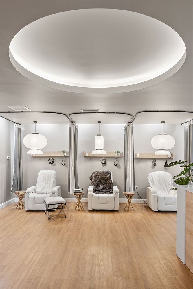 Modern spa lounge with white chairs, arched mirrors, and light wood flooring under a curved ceiling light