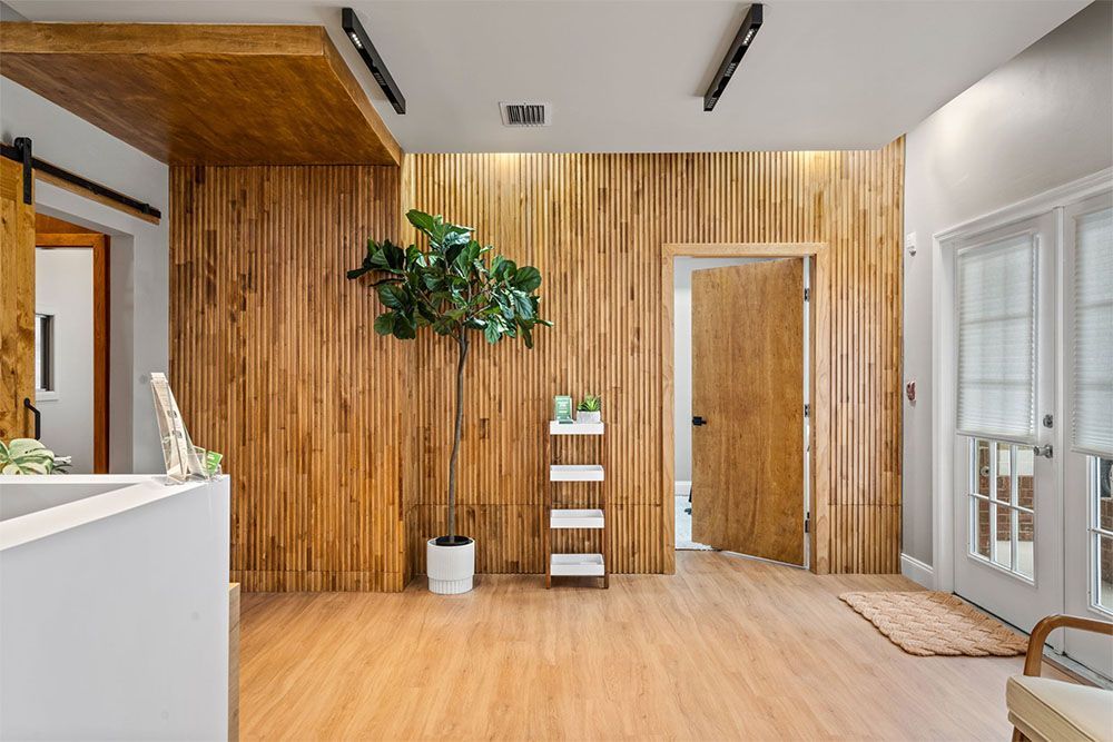 Bright lobby with wood-paneled wall, potted plant, small shelf, and glass doors on the right.