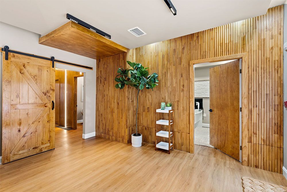 Modern room with light wood walls and floor, open barn doors, potted plant, and a small white shelf unit.