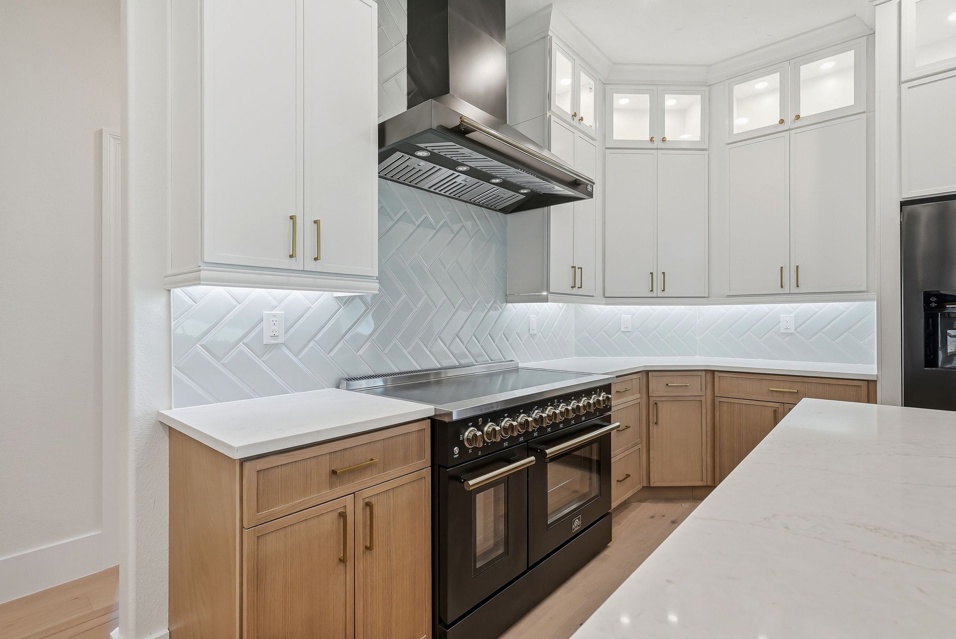 Kitchen range area with light wood cabinetry, black range, and white herringbone tile backsplash