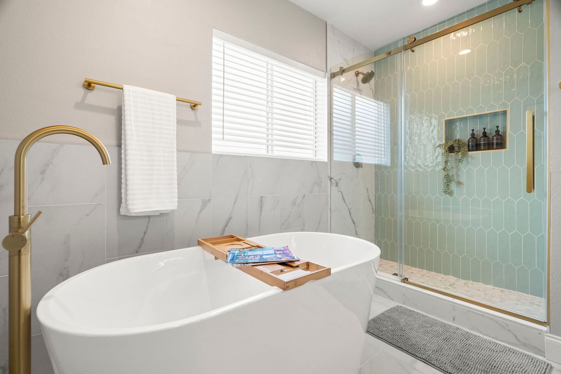 Luxury master bathroom remodel with a freestanding soaking tub, sage green elongated hexagon shower tile, glass sliding shower door, marble-look wall tile, and brushed gold fixtures.