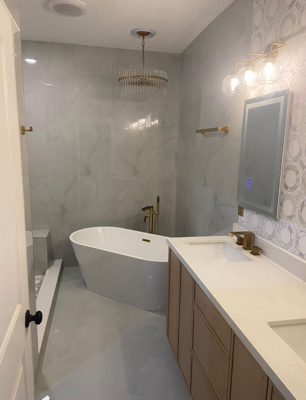 Luxury master bathroom remodel featuring a freestanding soaking tub, marble-look tile, gold fixtures, crystal chandelier, and custom double vanity by Step Up Home Improvements.