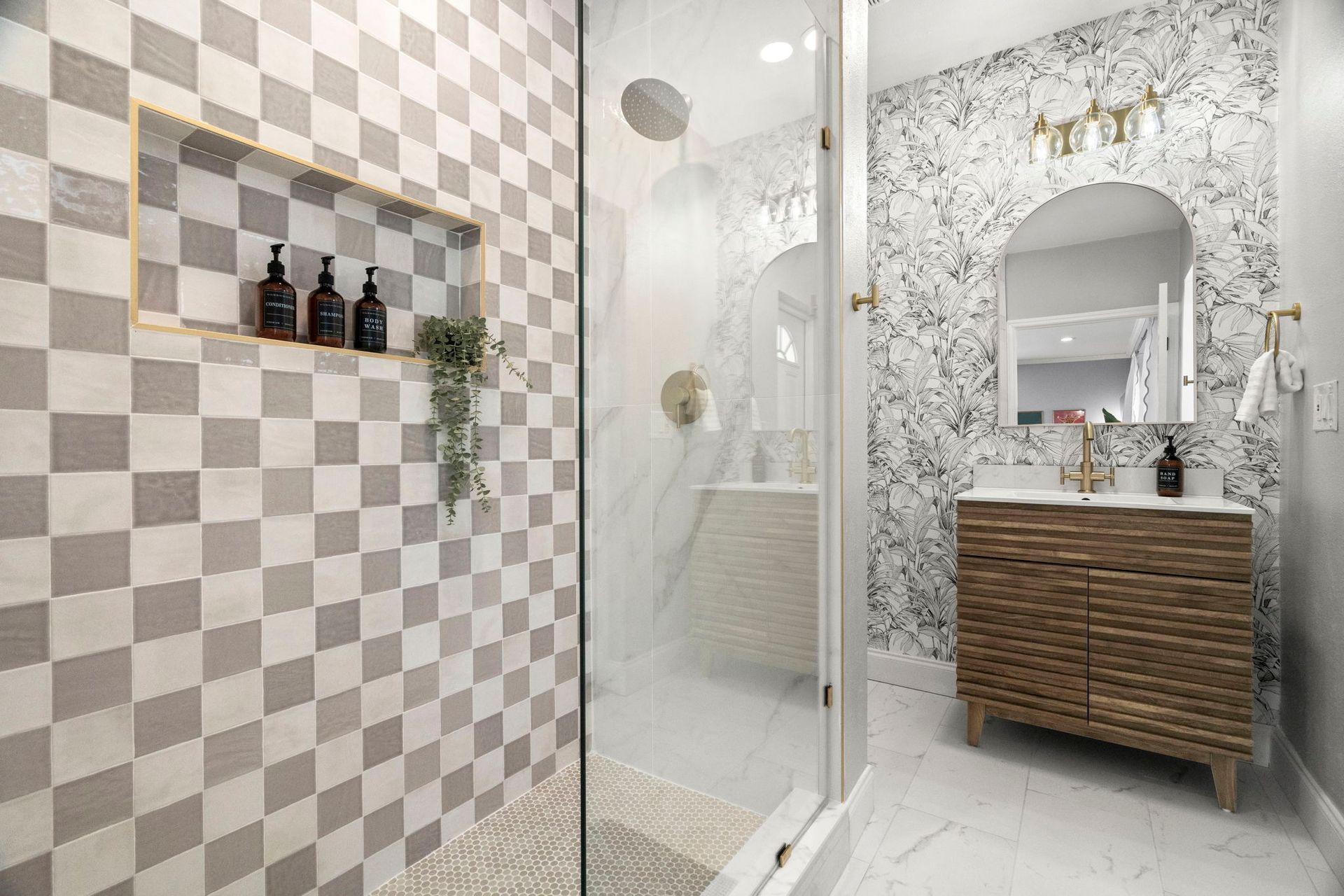 Modern bathroom remodel featuring gray and white checkerboard shower tile, a recessed niche, glass enclosure, floating wood vanity, and botanical wallpaper.