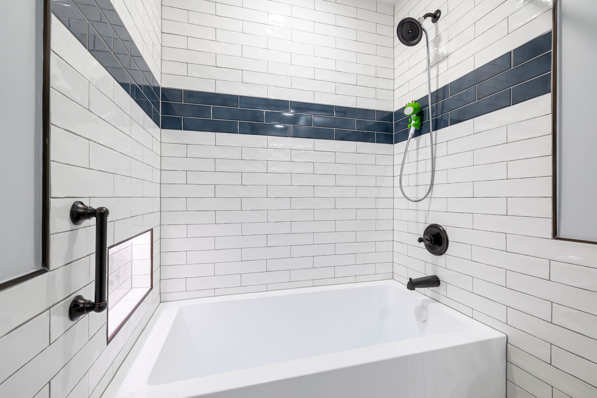 White tiled bathtub shower with dark blue accent strip and handheld showerhead
