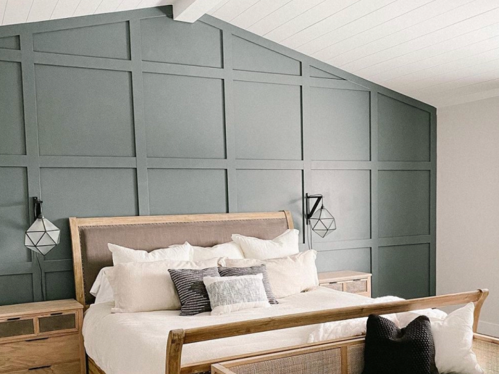 Modern bedroom with a gray paneled accent wall, wooden bed, white bedding, and black wall sconces