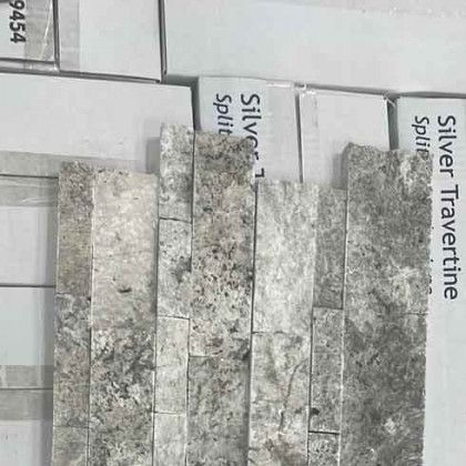 Stone tile samples in gray tones, stacked on a display board labeled “Silver Travertine Split.”