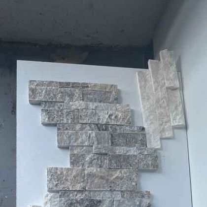 Stacked gray stone veneer panels arranged on a white board against a wall.