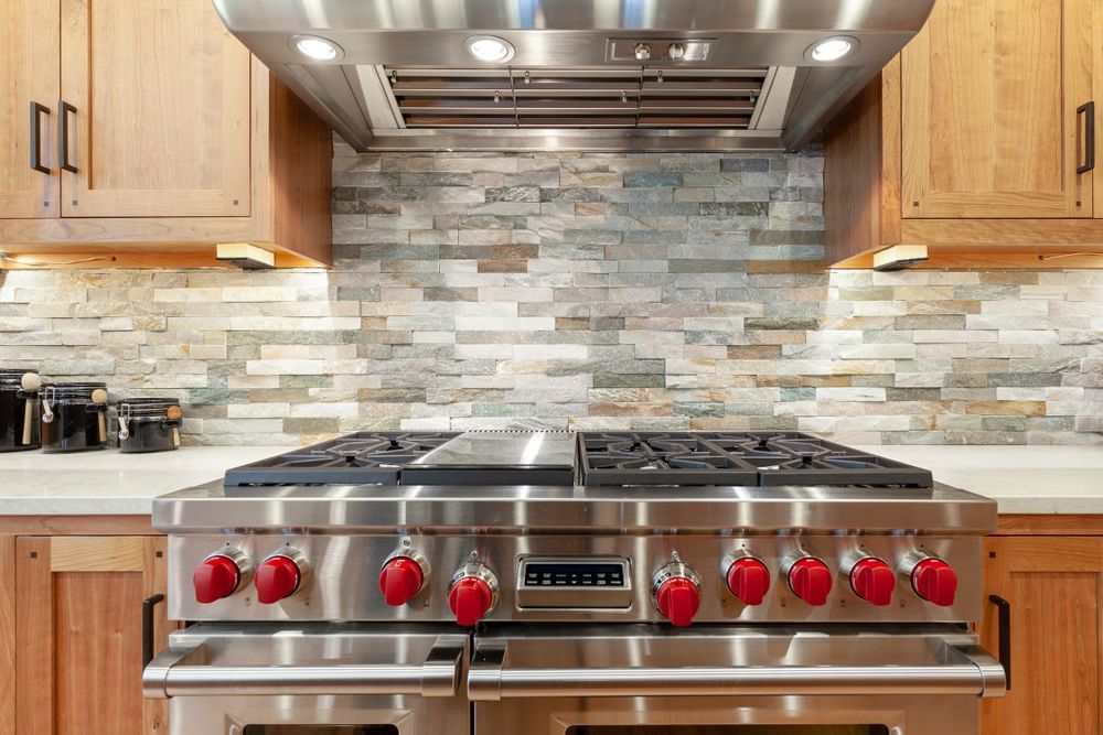 Modern kitchen with stainless steel range, red knobs, wood cabinets, and stone tile backsplash