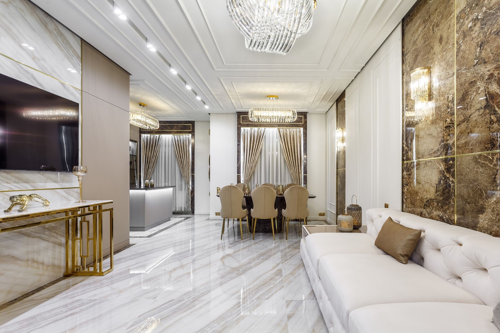 Luxury white living and dining room with marble floors, crystal chandeliers, and gold accents