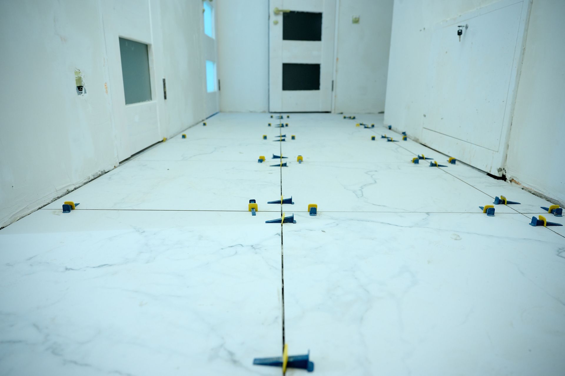 Empty white tiled room with floor level markers and door at the far end